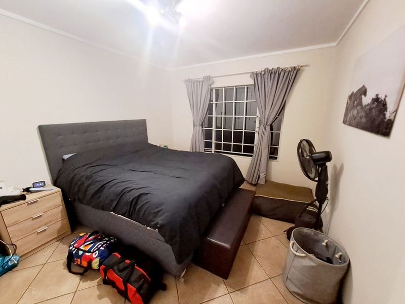 A functional bedroom featuring tiled flooring and a window fitted with security bars.