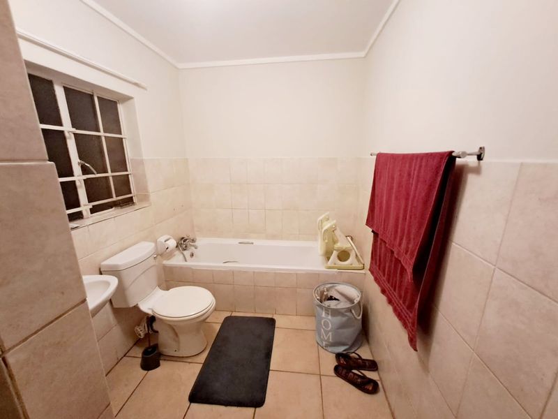 A functional bathroom featuring a bathtub, toilet, and washbasin with neutral wall and floor tiling and a window with security bars.