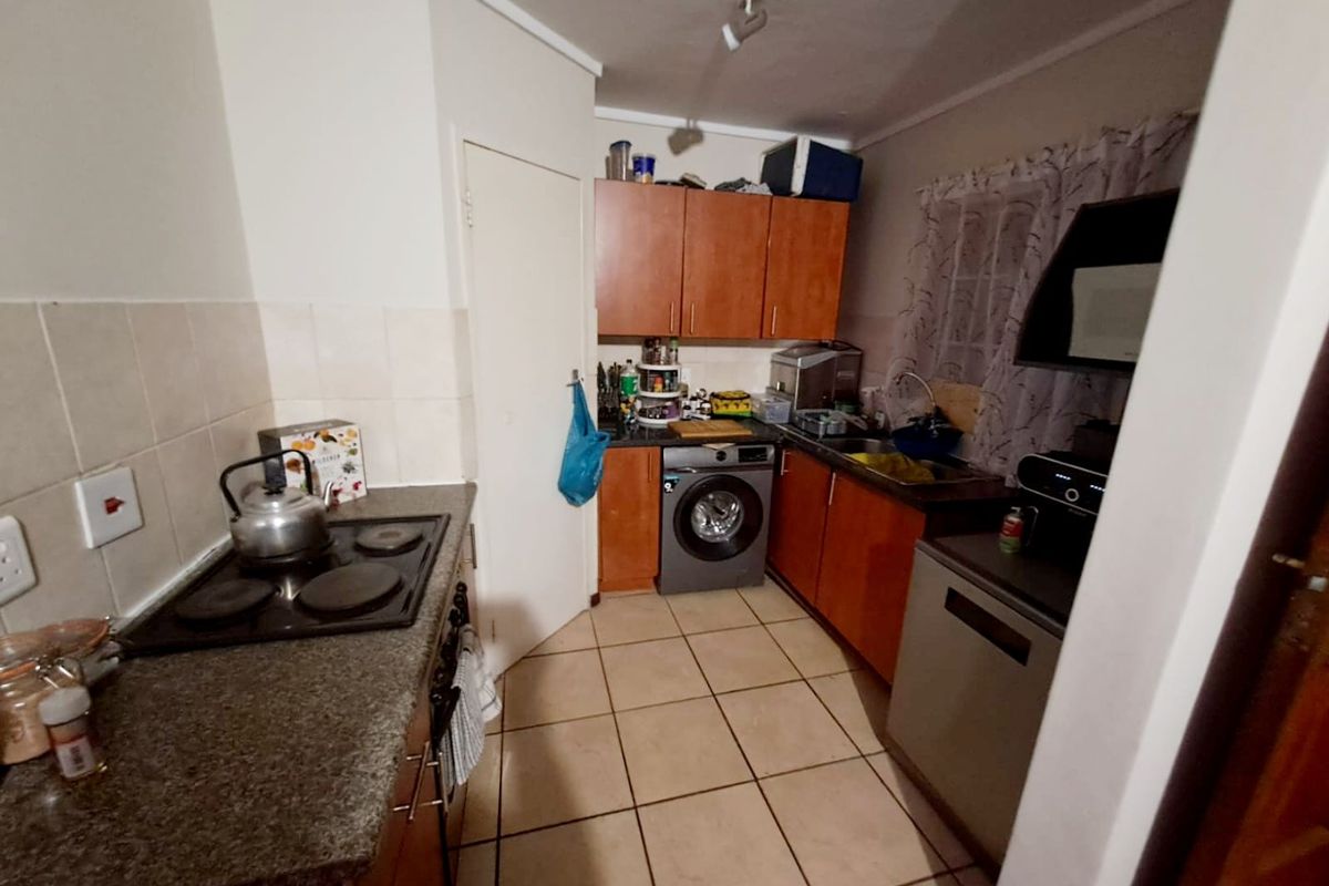 Compact kitchen featuring wooden cabinetry, laminate countertops, an electric hob, and integrated laundry facilities with tiled flooring and backsplash.