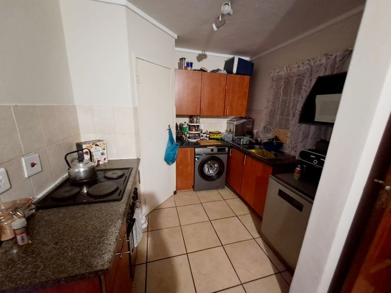 Compact kitchen featuring wooden cabinetry, laminate countertops, an electric hob, and integrated laundry facilities with tiled flooring and backsplash.