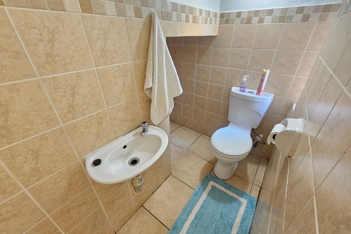 A compact guest bathroom featuring neutral ceramic wall and floor tiling, a wall-mounted basin, and a standard ceramic toilet.