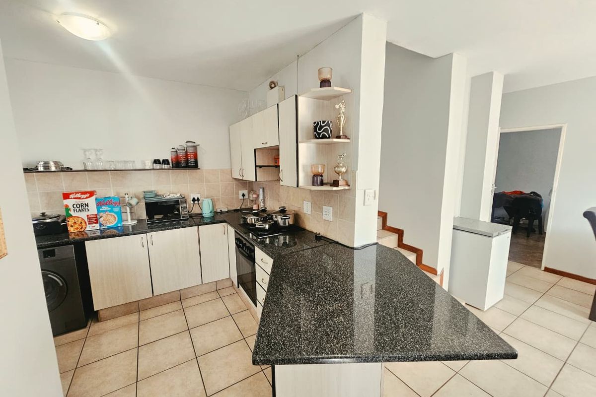 Functional kitchen featuring granite countertops, built-in cabinetry, a breakfast bar, and tiled flooring, with an open-plan layout leading to the living area.