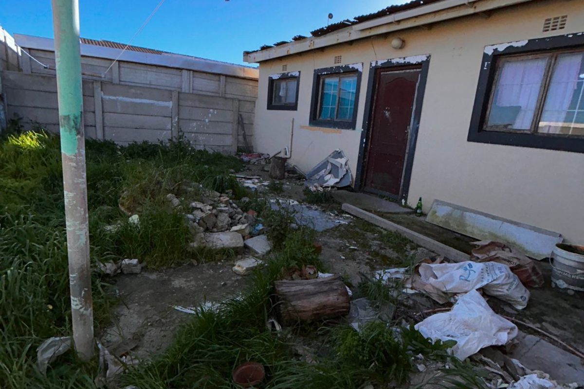 Rear exterior view of the property showing a concrete yard area with boundary walling and significant maintenance required to the building facade and grounds.