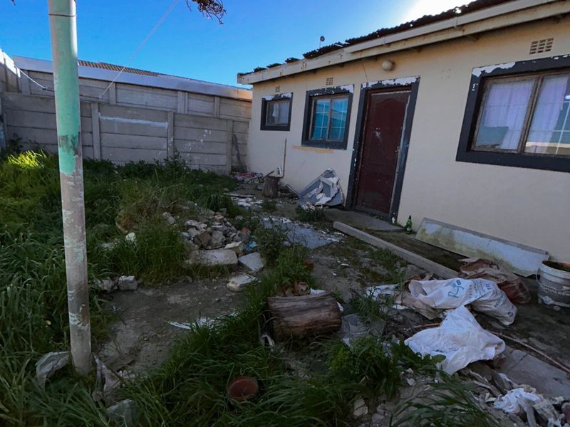 Rear exterior view of the property showing a concrete yard area with boundary walling and significant maintenance required to the building facade and grounds.
