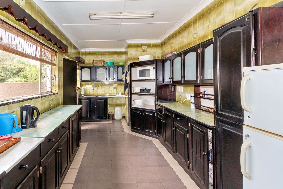A dated kitchen featuring dark cabinetry, extensive olive-toned wall tiling, tiled flooring, and ample counter space, offering significant potential for a modern renovation.