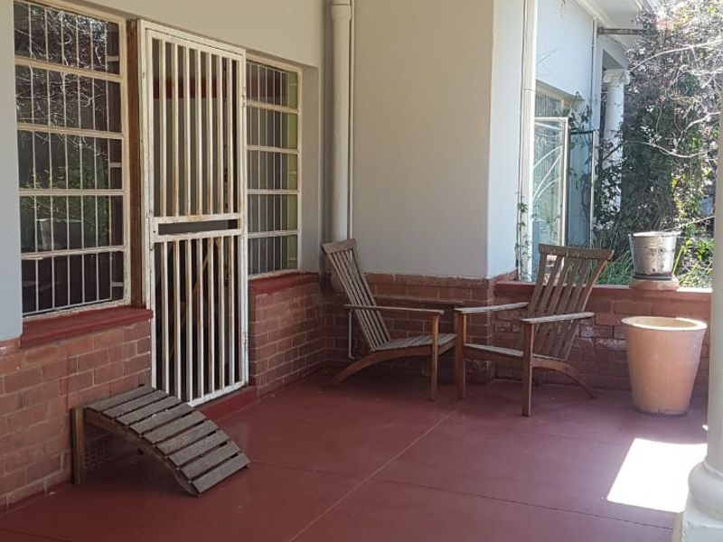 A covered patio area featuring painted concrete flooring, brick wall accents, and security fixtures, providing a functional outdoor space for relaxation.