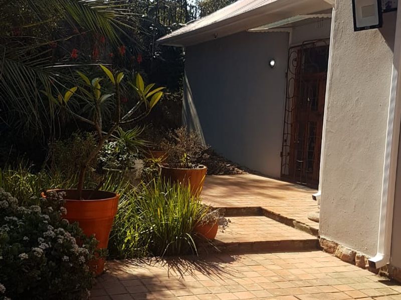A rear exterior view showing a terracotta tiled patio area leading to a side entrance with a security gate and external lighting.