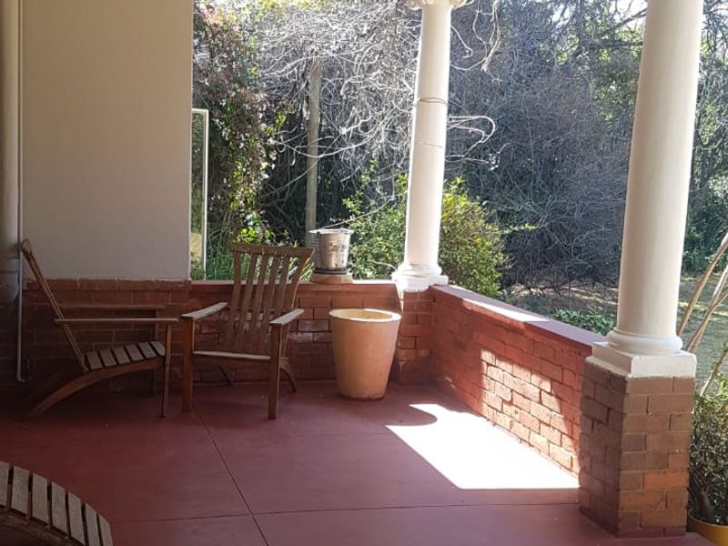 A covered patio featuring classic columns, a brick balustrade, and painted concrete flooring, offering a pleasant outdoor space overlooking the garden.