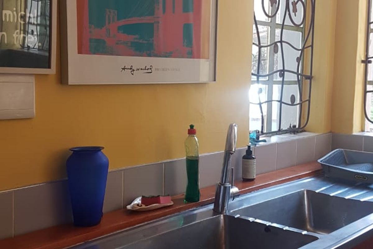 A kitchen sink area featuring a stainless steel double basin, wooden countertop, tiled splashback, and decorative wrought iron window security bars.