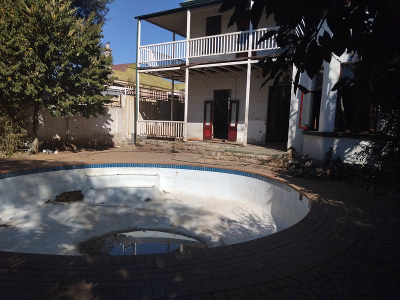 Rear exterior view featuring a two-story balcony and an empty swimming pool with surrounding brick paving and stone patio area.