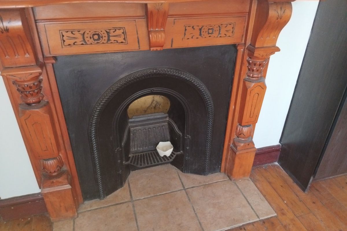 A classic living room feature showcasing an ornate timber fireplace mantel with a cast iron insert and tiled hearth, set against timber flooring.