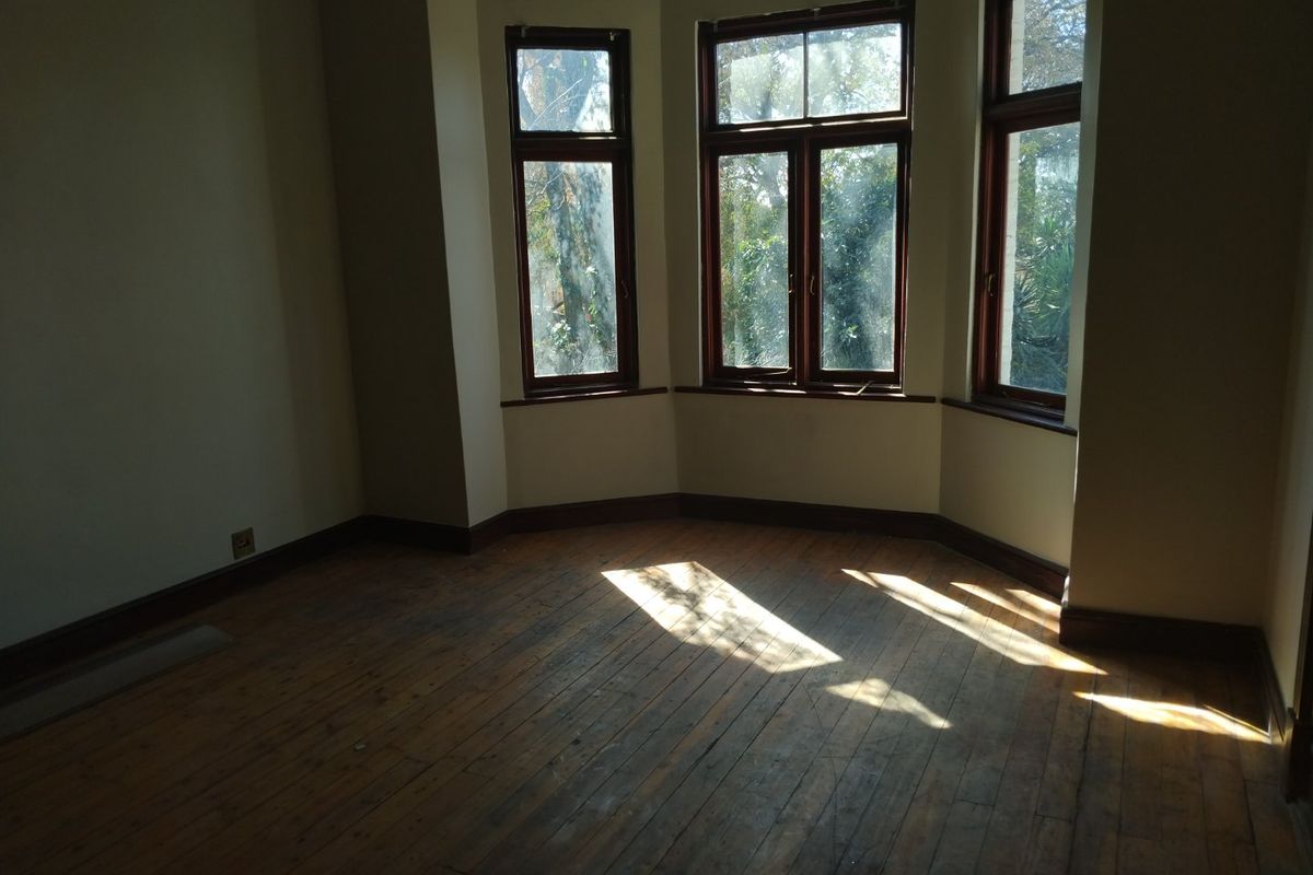 An empty bedroom featuring original timber flooring and a classic bay window, offering a bright space with potential for renovation.