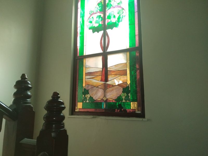 A hallway staircase area featuring a decorative stained glass window with a tree motif and a traditional timber balustrade.