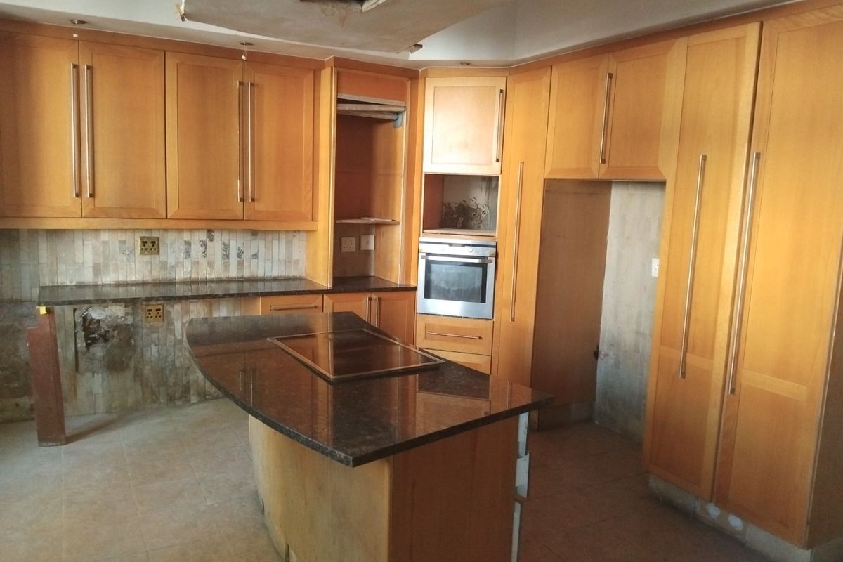 A spacious kitchen featuring wooden cabinetry, granite countertops, and a central island, currently requiring repairs to the ceiling and cabinetry finishes.
