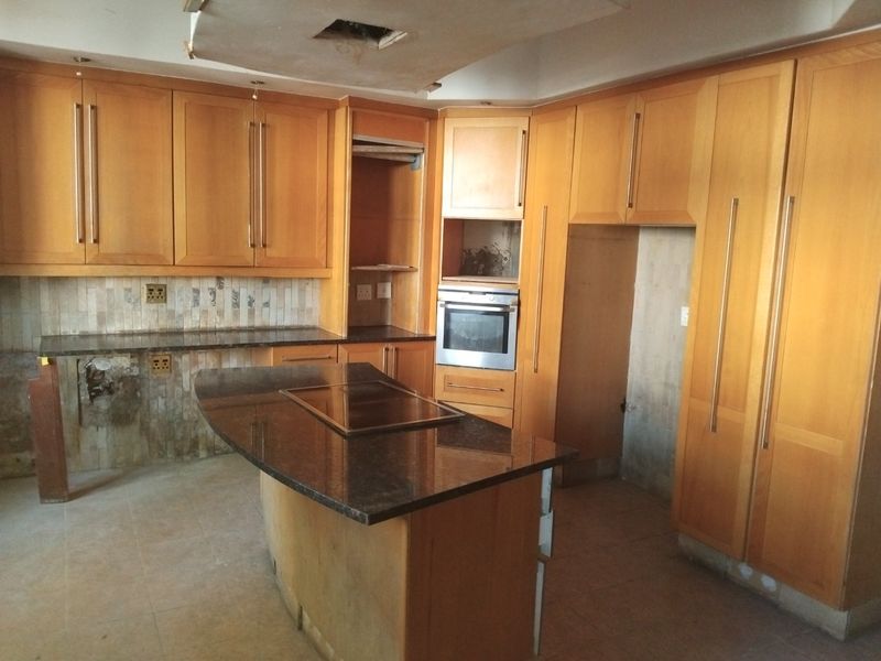 A spacious kitchen featuring wooden cabinetry, granite countertops, and a central island, currently requiring repairs to the ceiling and cabinetry finishes.