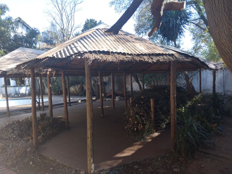 An outdoor covered patio area featuring a thatched and corrugated metal roof supported by timber posts, situated in a garden setting.