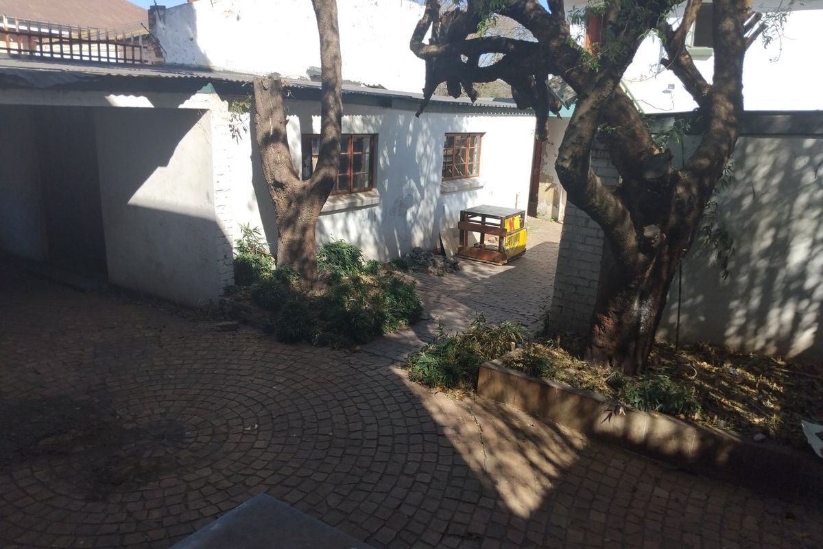 A rear courtyard area featuring paved flooring, mature trees, and exterior building access with visible wear to the finishes.