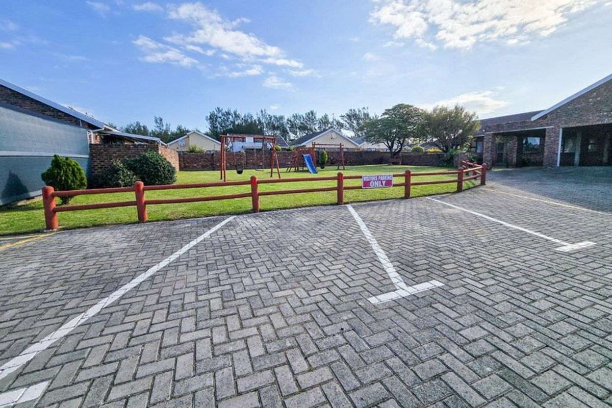 A paved visitor parking area adjacent to a communal lawn with a timber fence and brick boundary wall.