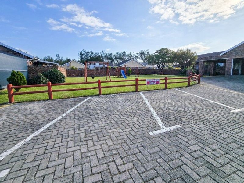 A paved visitor parking area adjacent to a communal lawn with a timber fence and brick boundary wall.