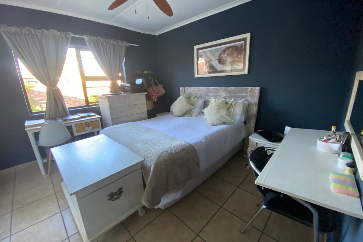 A bedroom featuring dark painted walls, tiled flooring, and a ceiling fan, providing a functional space with natural light from the window.