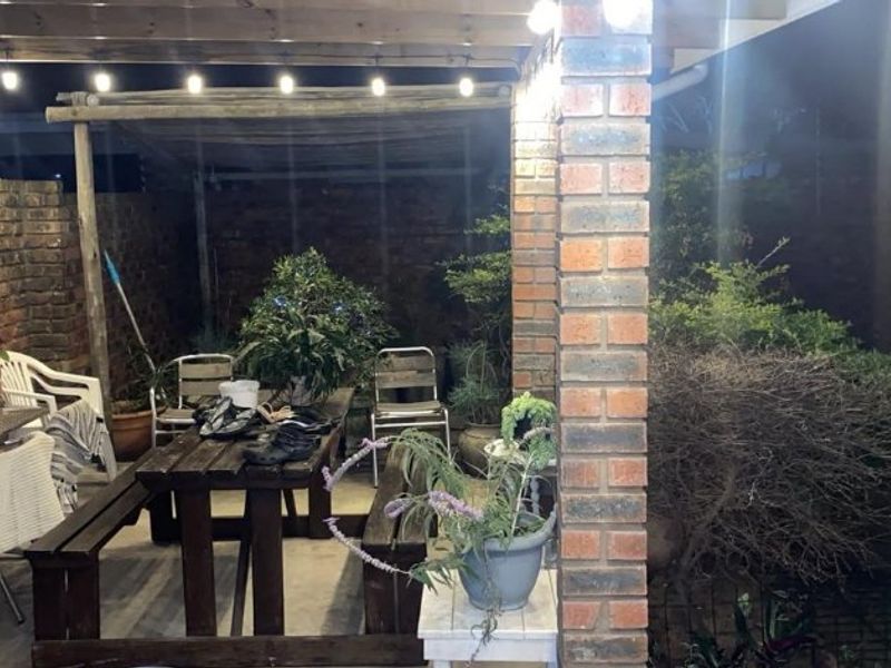 A covered outdoor patio area featuring exposed brick pillars, a timber pergola structure, and concrete flooring, suitable for evening outdoor dining and relaxation.