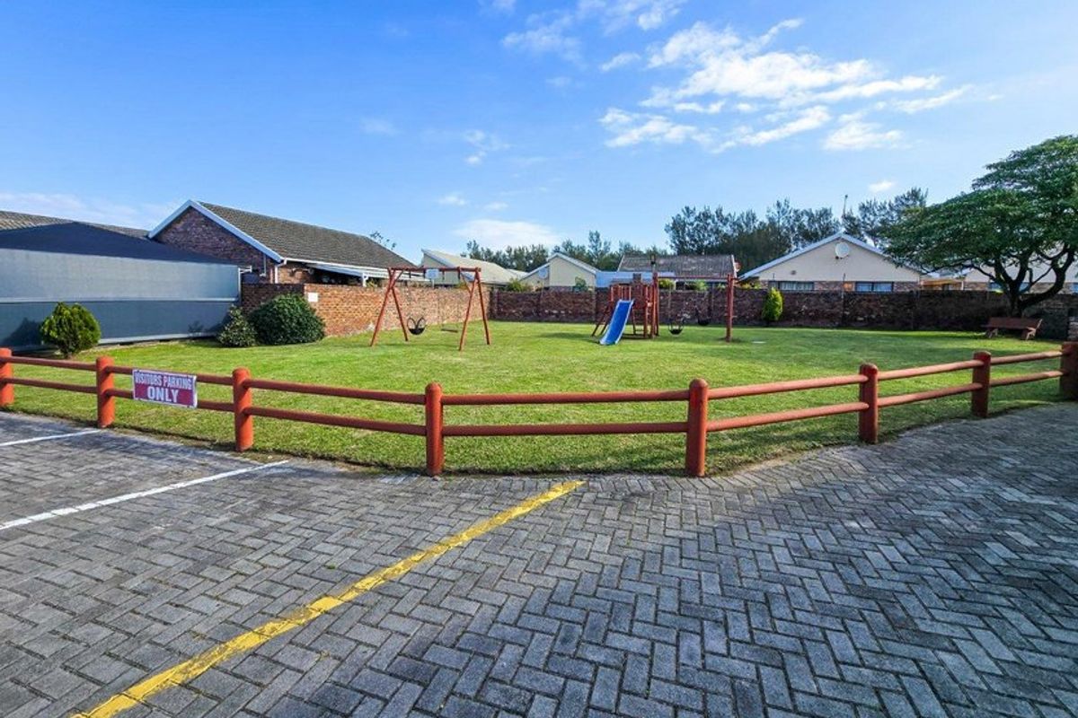 A well-maintained communal garden area featuring a lawn, brick boundary walls, and a paved parking area with visitor bays.