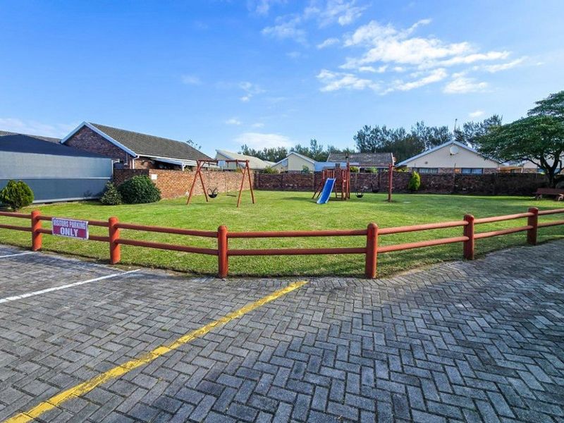 A well-maintained communal garden area featuring a lawn, brick boundary walls, and a paved parking area with visitor bays.