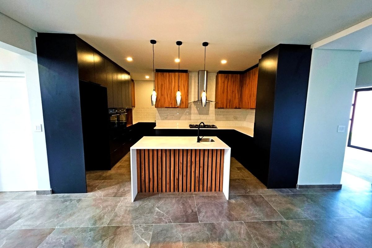 Modern kitchen featuring a central island, sleek dark cabinetry, wood-accented cupboards, stone countertops, and high-end built-in appliances with contemporary lighting.