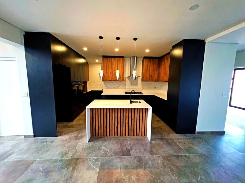 Modern kitchen featuring a central island, sleek dark cabinetry, wood-accented cupboards, stone countertops, and high-end built-in appliances with contemporary lighting.