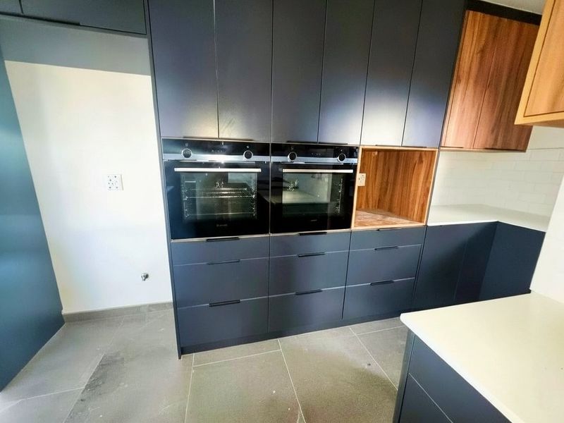 Modern kitchen featuring dark cabinetry, built-in double ovens, stone countertops, and a subway tile backsplash, presenting a clean and contemporary aesthetic.