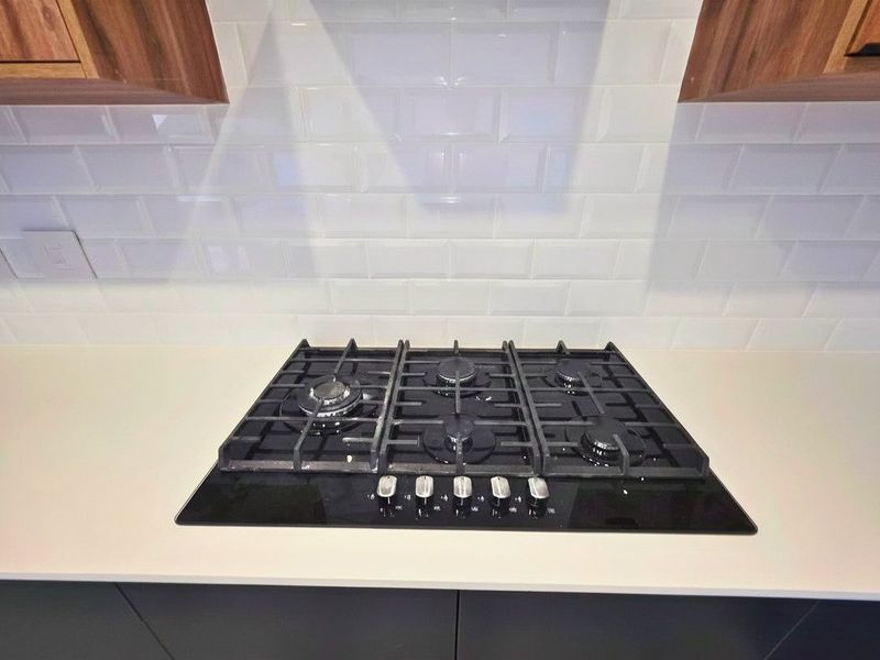 A modern kitchen featuring a built-in gas cooktop set into a stone countertop with a clean white subway tile backsplash.