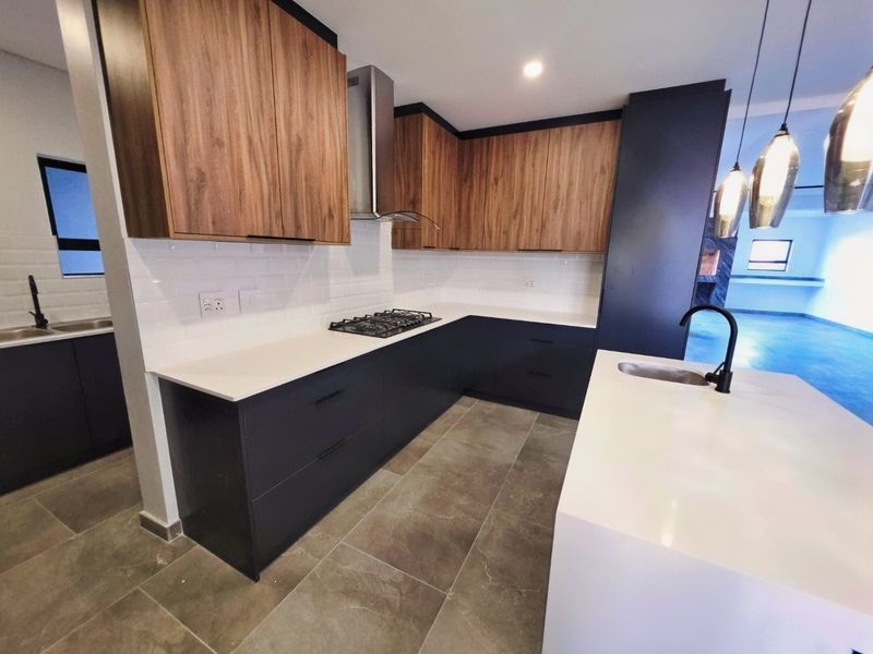 Modern kitchen featuring two-tone cabinetry, stone countertops, a central island with sink, gas hob, and stylish subway tile backsplash.
