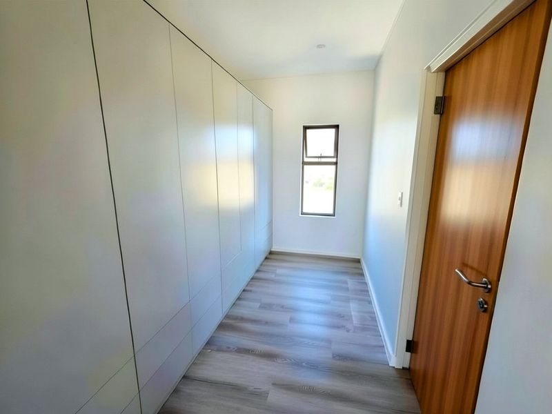 A clean, modern hallway featuring extensive built-in cabinetry, light wood-look laminate flooring, and a contemporary timber door.