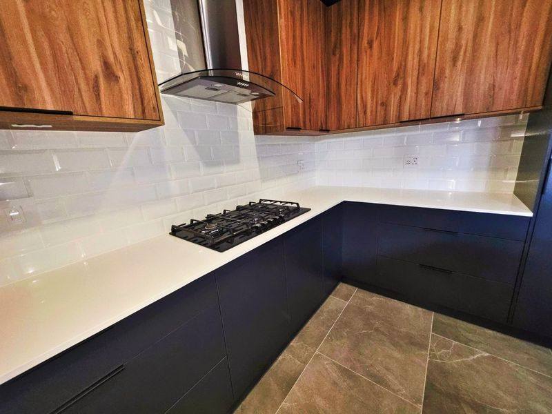 Modern kitchen featuring dark lower cabinetry, wood-tone upper cabinets, white stone countertops, a gas cooktop, and a stylish subway tile backsplash.