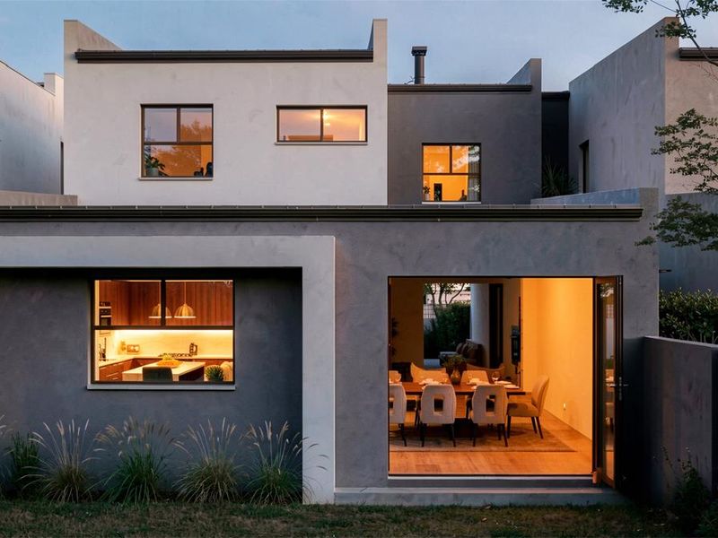 A modern rear elevation of a two-story house featuring contemporary plaster finishes, large bi-fold doors, and well-maintained exterior lighting.