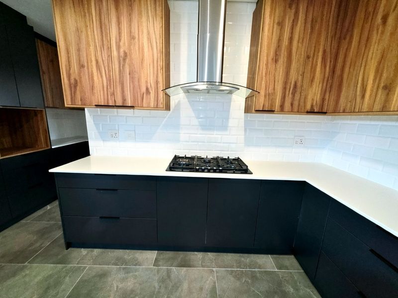 Modern kitchen featuring dark cabinetry, wood-grain upper cabinets, white quartz countertops, subway tile backsplash, and a stainless steel extractor fan.
