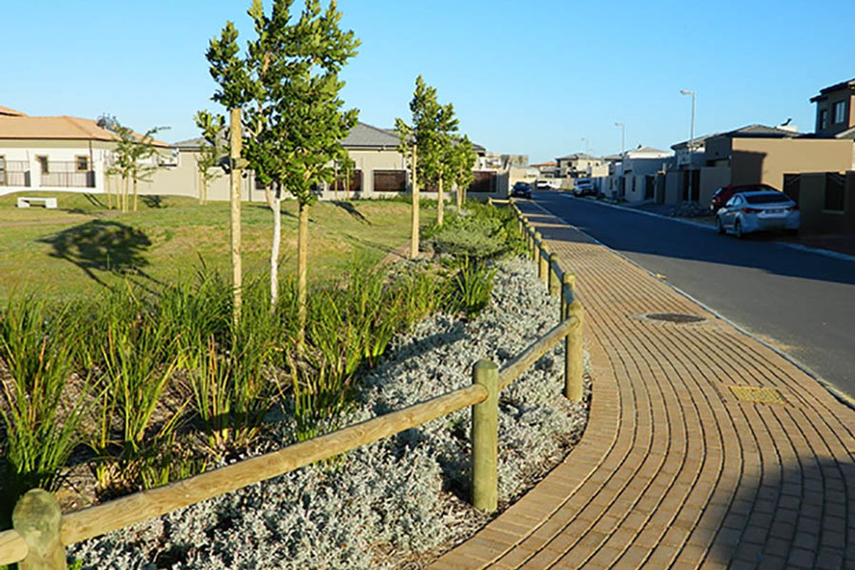 A view of a residential street featuring a paved sidewalk, timber fencing, and landscaped verge area within a suburban estate.