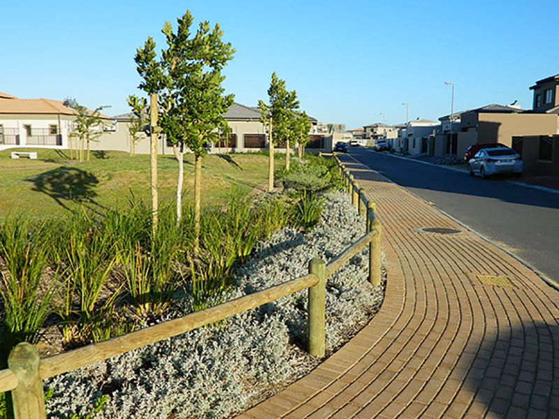 A view of a residential street featuring a paved sidewalk, timber fencing, and landscaped verge area within a suburban estate.