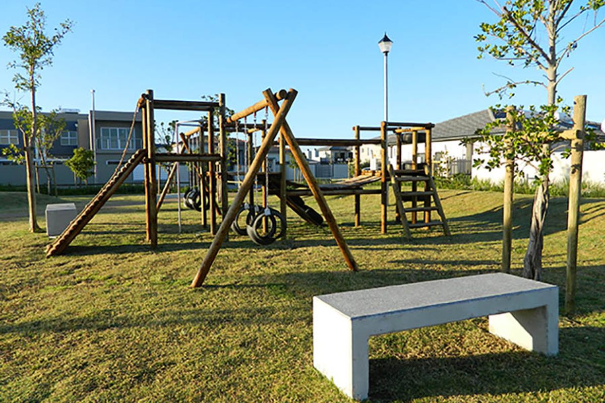 A well-maintained communal garden area featuring a wooden playground structure, a concrete bench, and established landscaping.