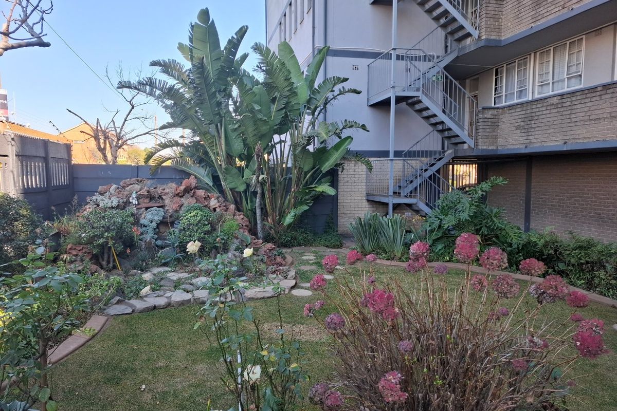 A well-maintained rear garden area featuring a rockery, established plants, and access to the building's external metal fire escape staircase.