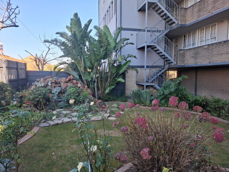 A well-maintained rear garden area featuring a rockery, established plants, and access to the building's external metal fire escape staircase.