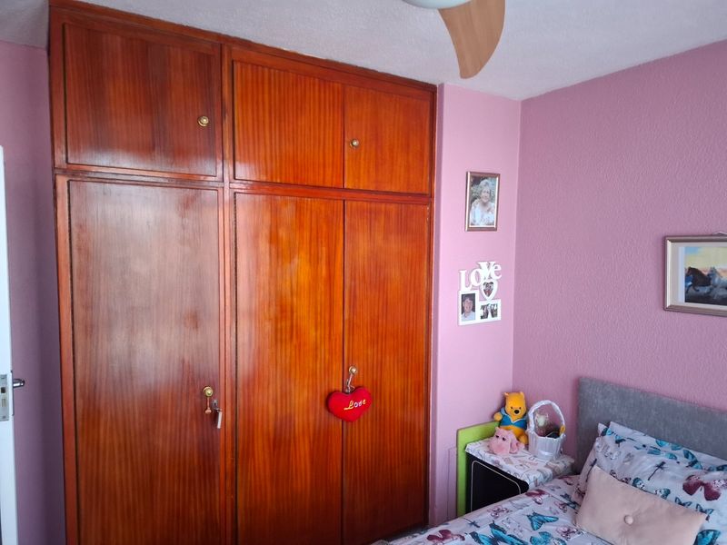 A bedroom featuring a large, full-height built-in wooden wardrobe and a ceiling fan, finished with pink wall paint.