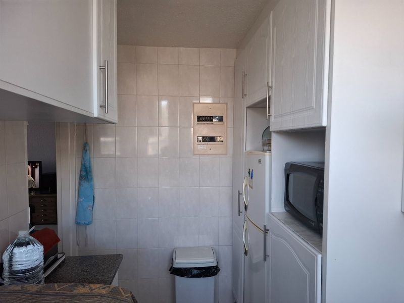 A compact kitchen area featuring white built-in cabinetry, tiled wall finishes, and a dedicated housing unit for a microwave.
