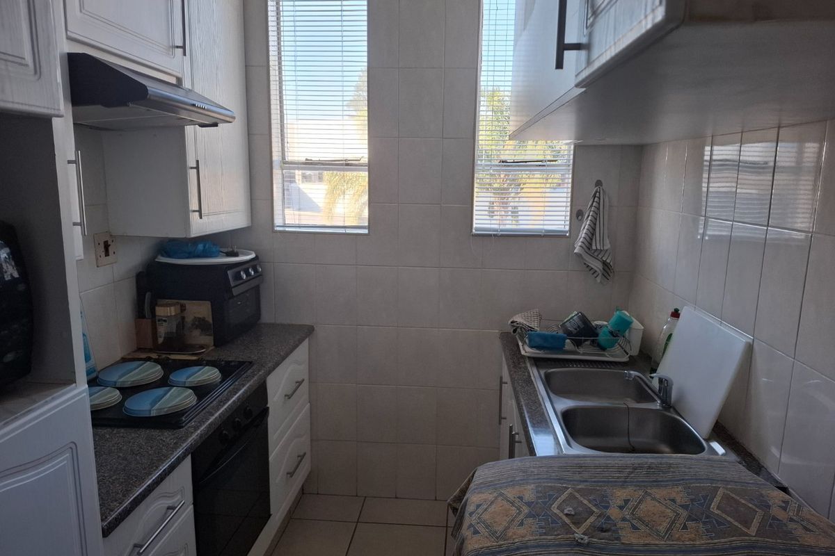 Compact kitchen featuring white cabinetry, laminate countertops, a double stainless steel sink, built-in oven, and electric hob with an extractor fan.