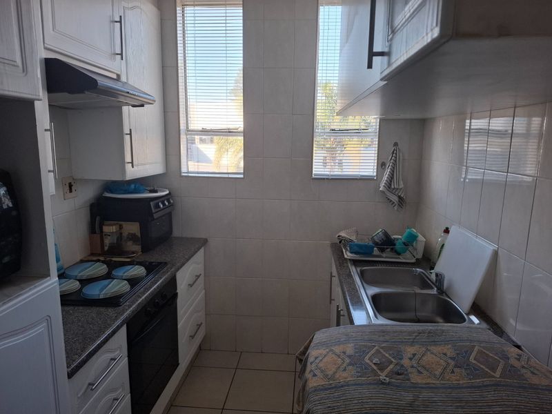 Compact kitchen featuring white cabinetry, laminate countertops, a double stainless steel sink, built-in oven, and electric hob with an extractor fan.