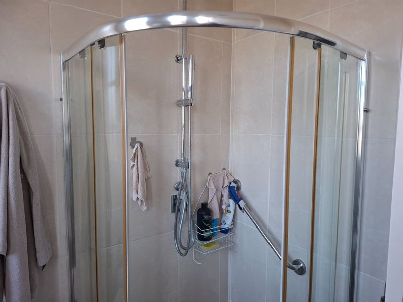 A functional bathroom shower area featuring a curved glass enclosure, chrome shower fittings, and a safety grab rail installed on tiled walls.