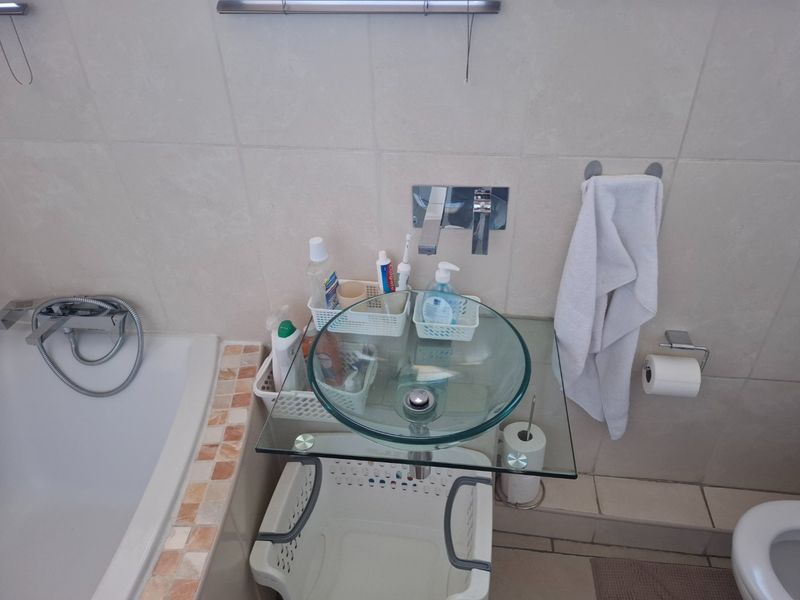 A compact bathroom featuring a glass vessel sink with wall-mounted faucet, tiled walls, and a built-in bathtub with shower attachment.