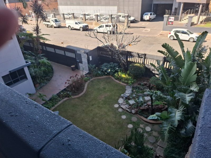 An elevated view of a private rear garden featuring a landscaped lawn, stone pathway, and paved walkway, enclosed by perimeter fencing.