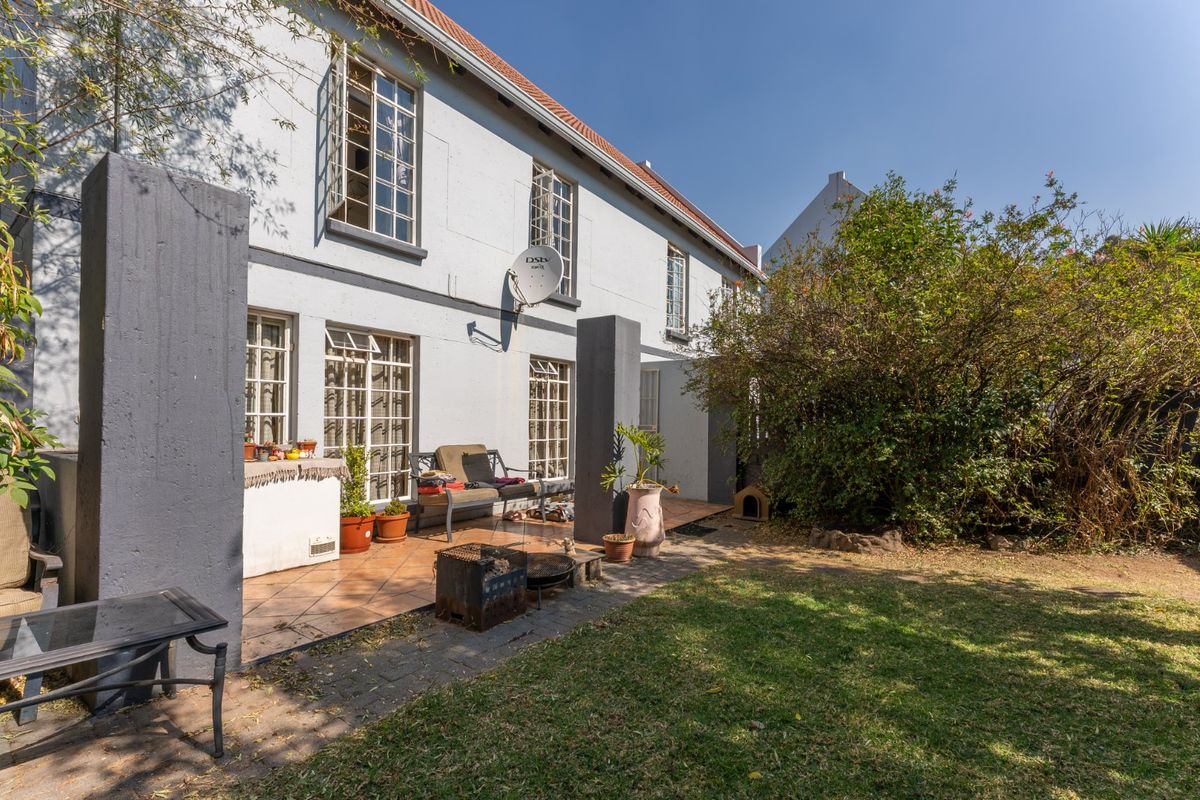 Rear view of the townhouse featuring a tiled patio area, established garden, and multi-pane windows set against a painted masonry facade.