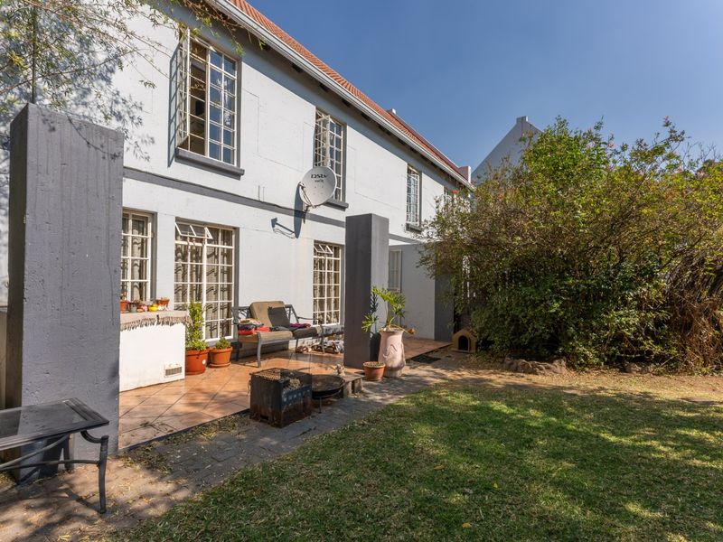 Rear view of the townhouse featuring a tiled patio area, established garden, and multi-pane windows set against a painted masonry facade.
